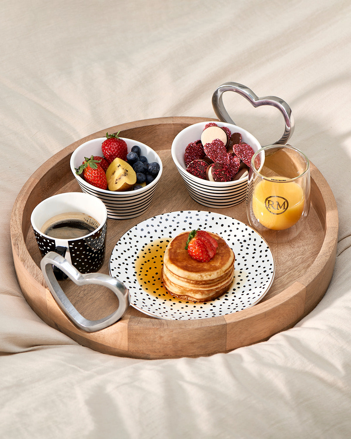 SERVING TRAY round  is made of mango wood heart-shaped handles made of glossy aluminum, decorated with tableware and some food, coffee, and juice by Riviera Maison