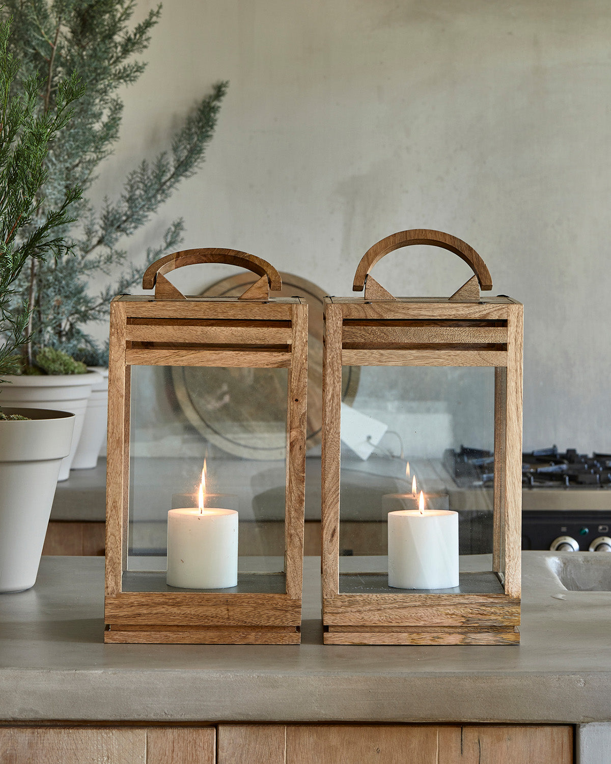 Two LANTERNS constructed from glass and wood with candles on its iron base by Riviera Maison